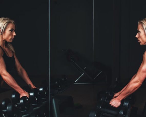 Athletic woman engaging in strength training exercise with dumbbells in a gym setting, reflecting on progress.